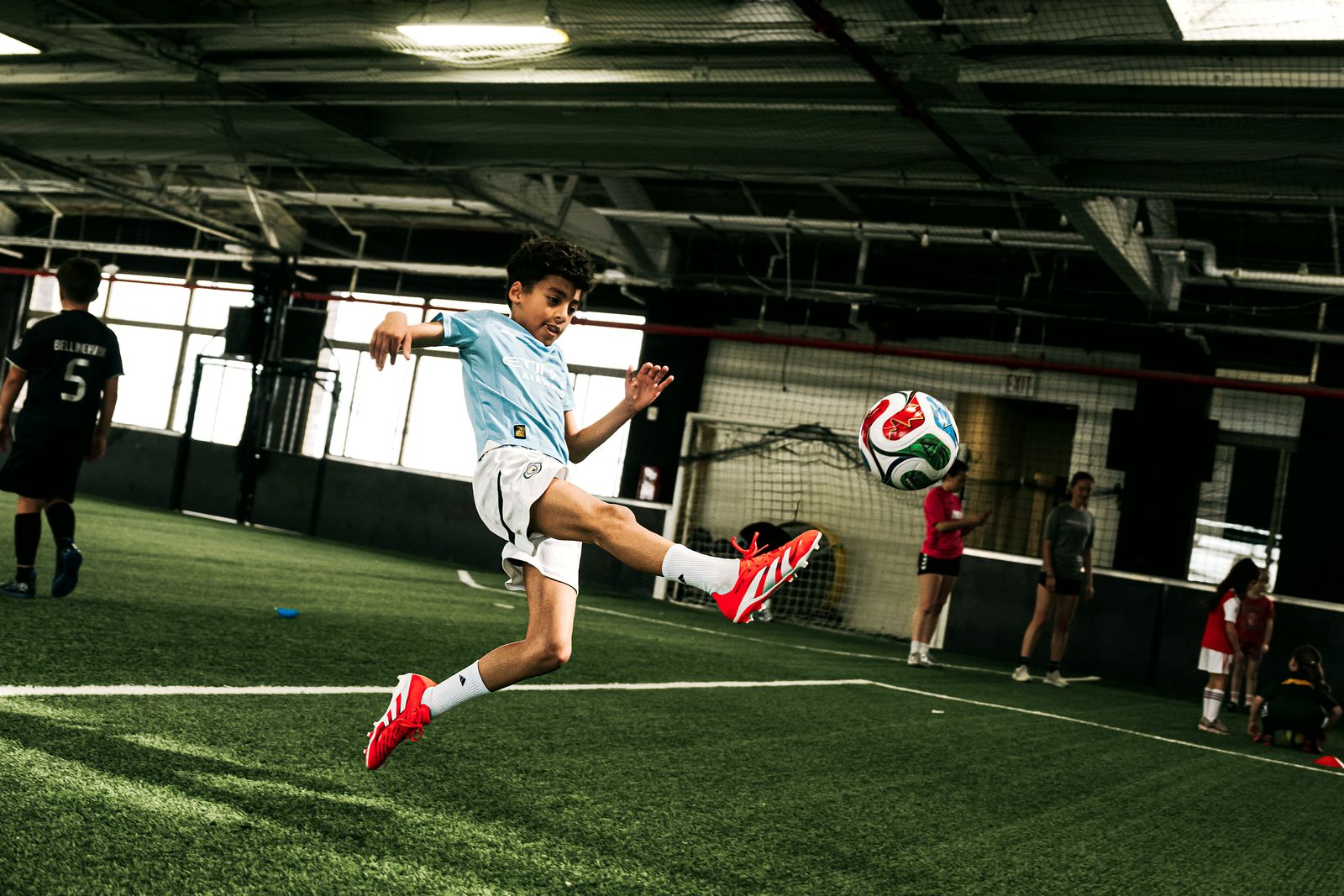 Young soccer player volleying the ball mid-air during training at Arena One.