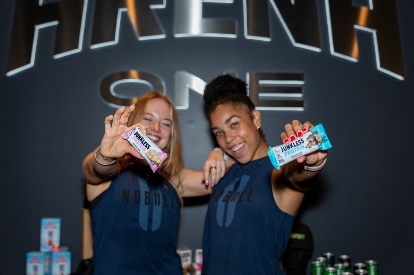 Two League members holding protein bars at the sponsor table.