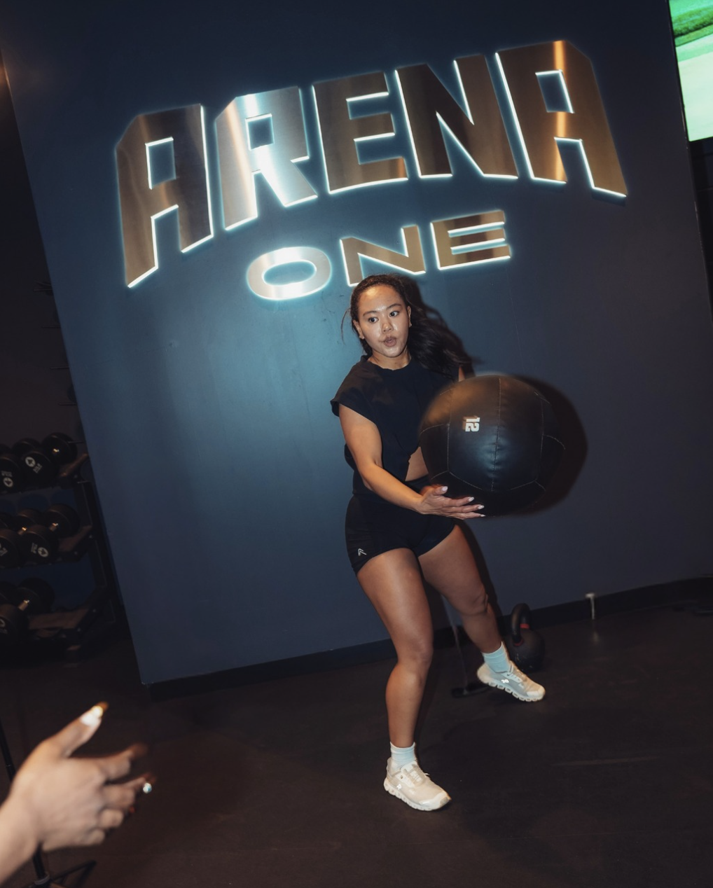 An athlete training with a medicine ball beneath the Arena One sign.